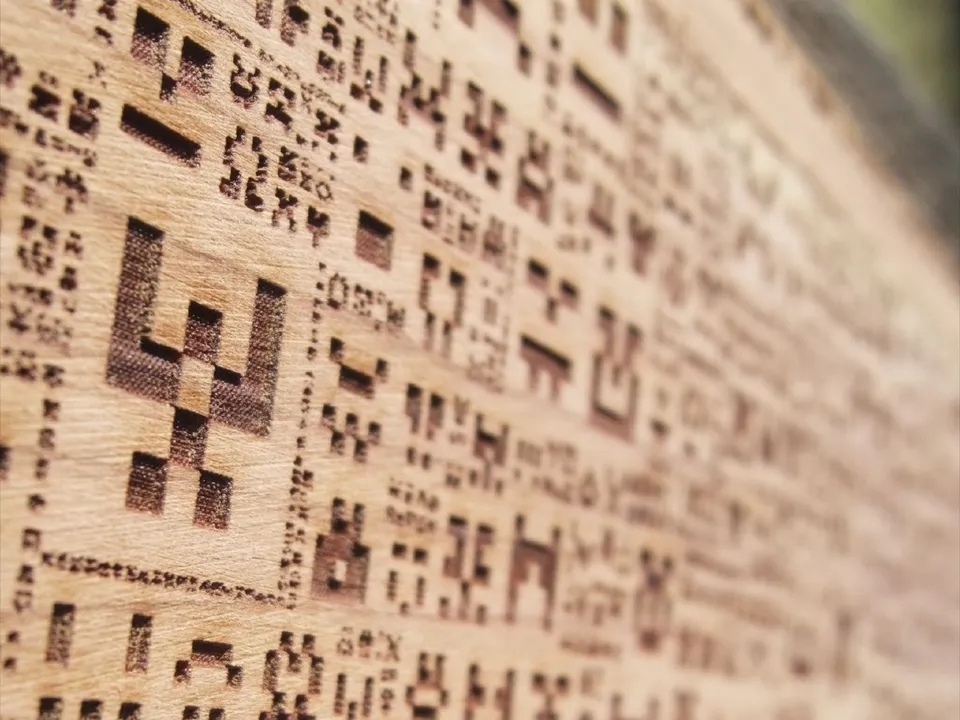 A cedar board with rows of pixelated, algorithm-generated invader shapes raster-engraved into it on an Epilog laser engraver.