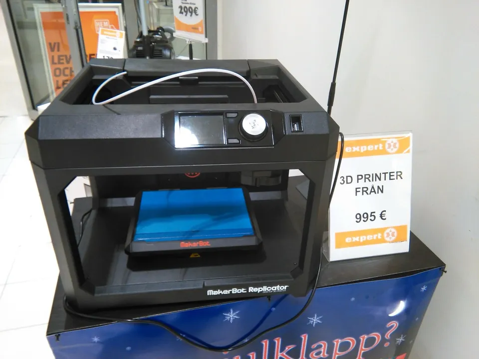 A MakerBot Replicator on a Christmas display in an Expert electronics store in Mariehamn, beside a sign offering 3D printers from €995.