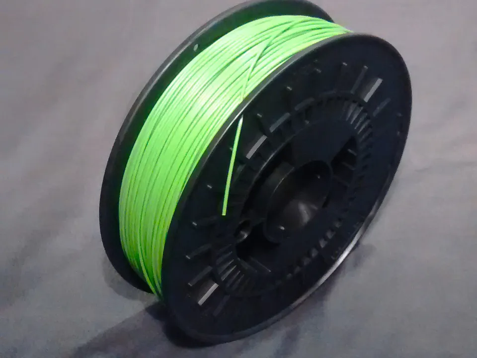 A spool of light green ABS filament on a black plastic reel, with the loose end tucked into the reel's side, lying on a grey cloth.