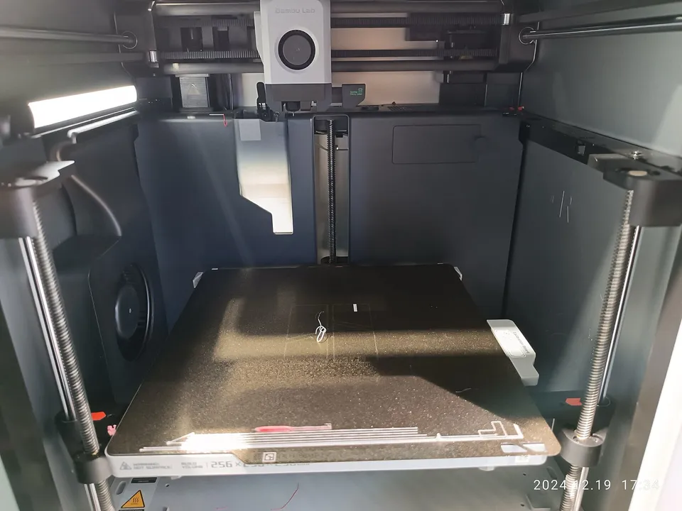 The open build chamber of an enclosed Bambu Lab printer in a store showroom, its textured plate lowered below the toolhead.