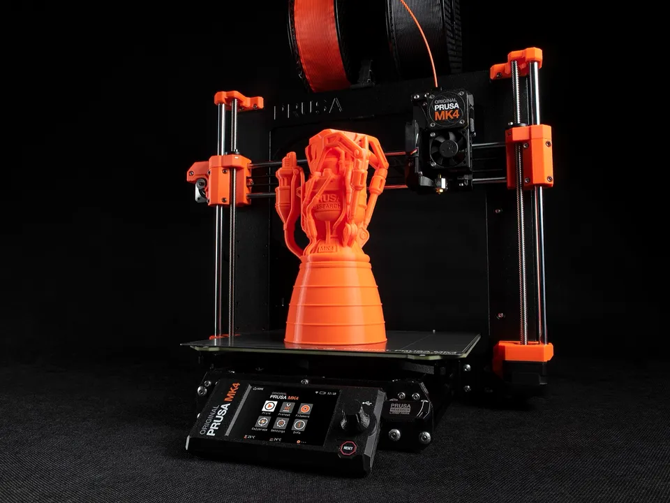 An Original Prusa MK4 bed-slinger with an orange printed rocket-engine model on its bed, against a black backdrop.