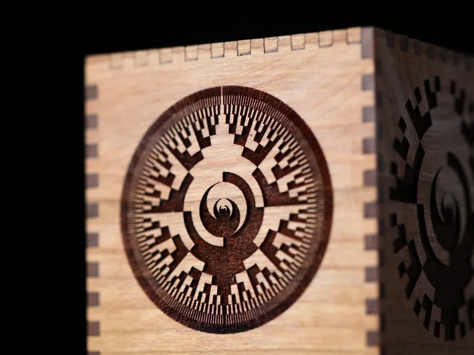 A finger-jointed cherry wood box with a circular binary pattern laser-engraved into its side.