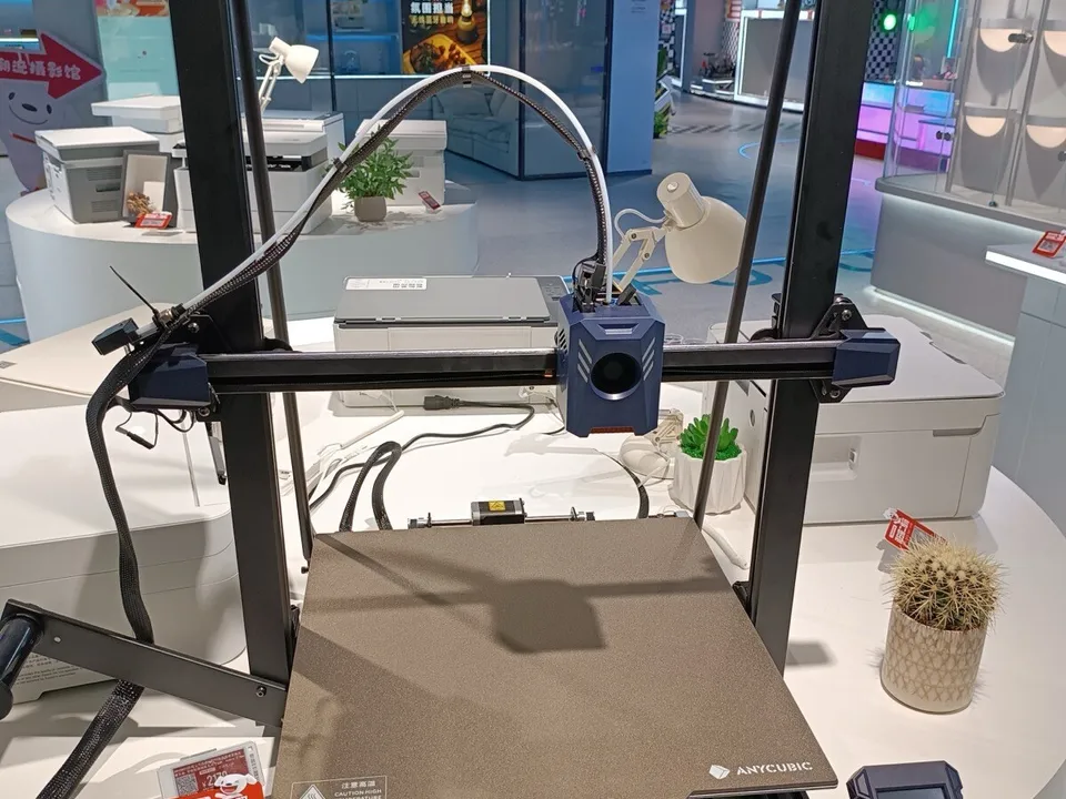 An open-frame Anycubic Kobra 2 Max on display at an electronics showroom in Dongguan, China, with a red electronic price tag beside its print bed.