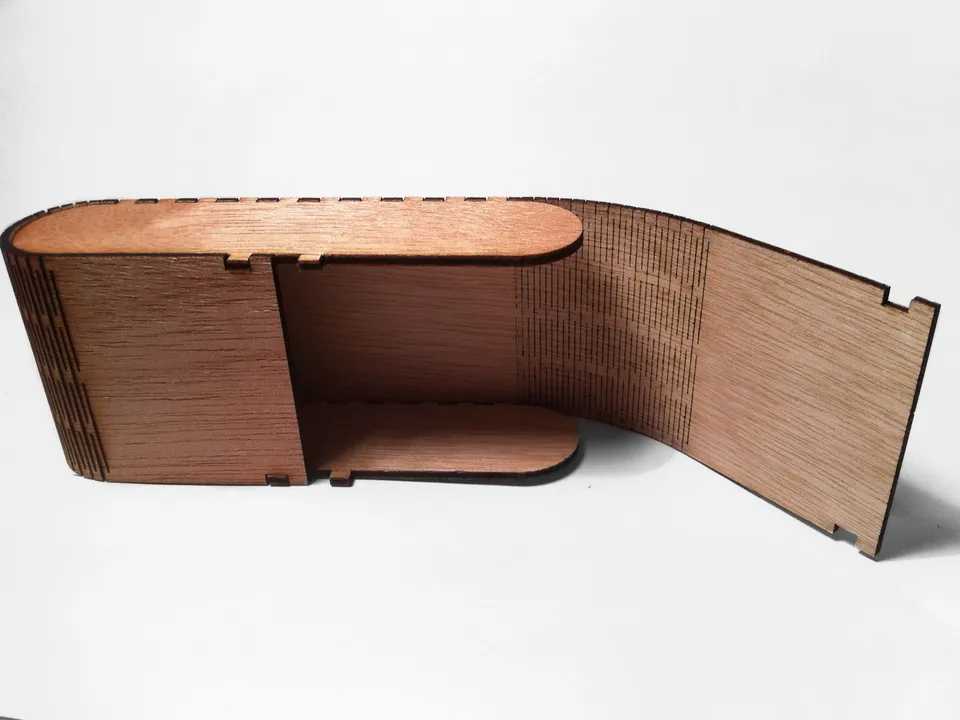 An oval plywood box laser cut with finger joints, its side wall bent open on a living hinge of parallel kerf cuts.