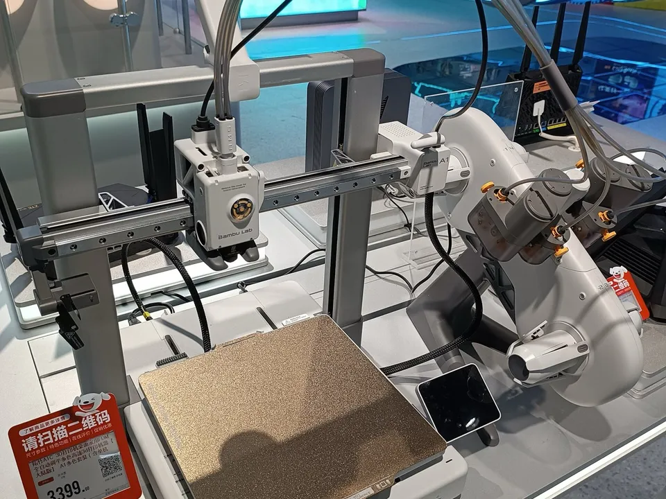 A Bambu Lab A1 on a store display: the toolhead rides an aluminum gantry above a textured build plate that slides front to back, with an AMS lite spool holder beside it.