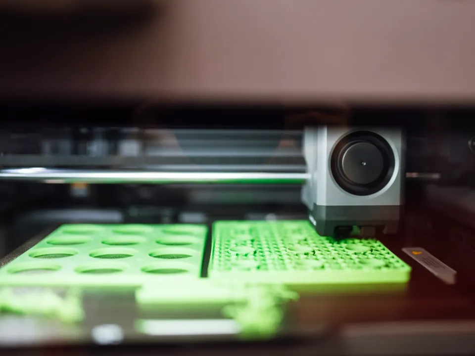 Two large flat green parts printing side by side on the bed of a 3D printer, with the toolhead over the right-hand part.