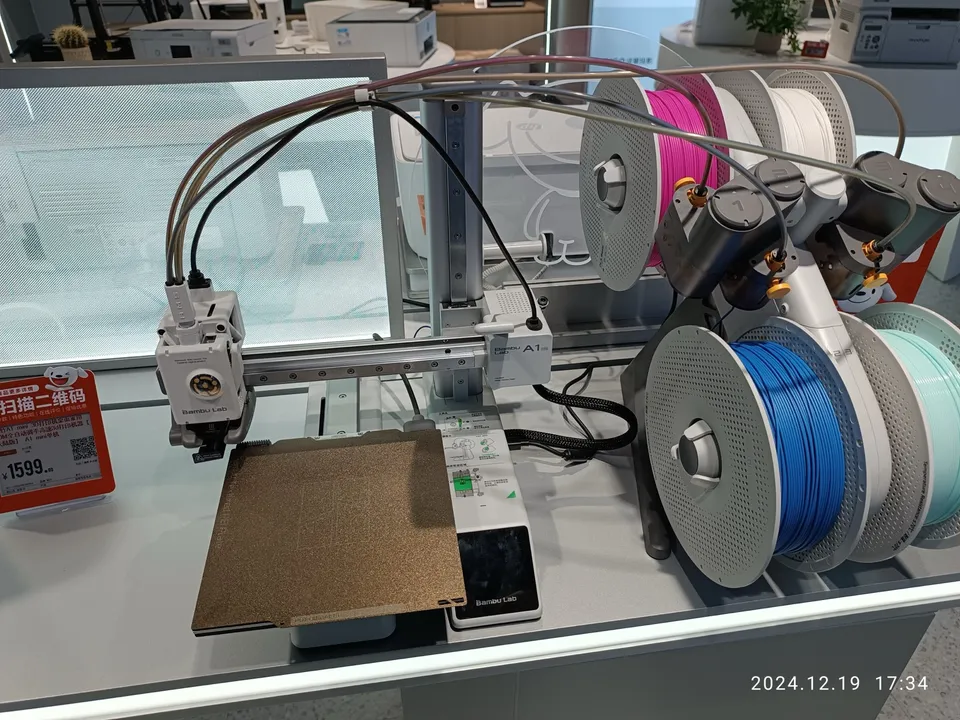 A Bambu Lab A1 mini on a store display, its empty textured build plate in front and an AMS lite holding four spools beside it