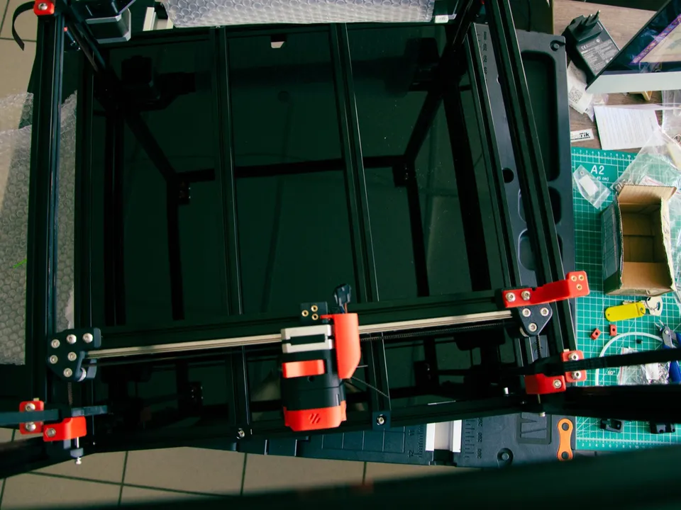 Top-down view of a Voron CoreXY printer under assembly, showing the X rail, the toolhead carriage and the belt idlers at each end of the gantry.
