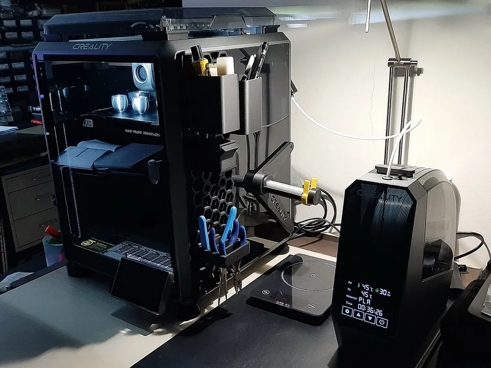 An enclosed Creality K1C CoreXY printer on a workbench, next to a filament dry box.