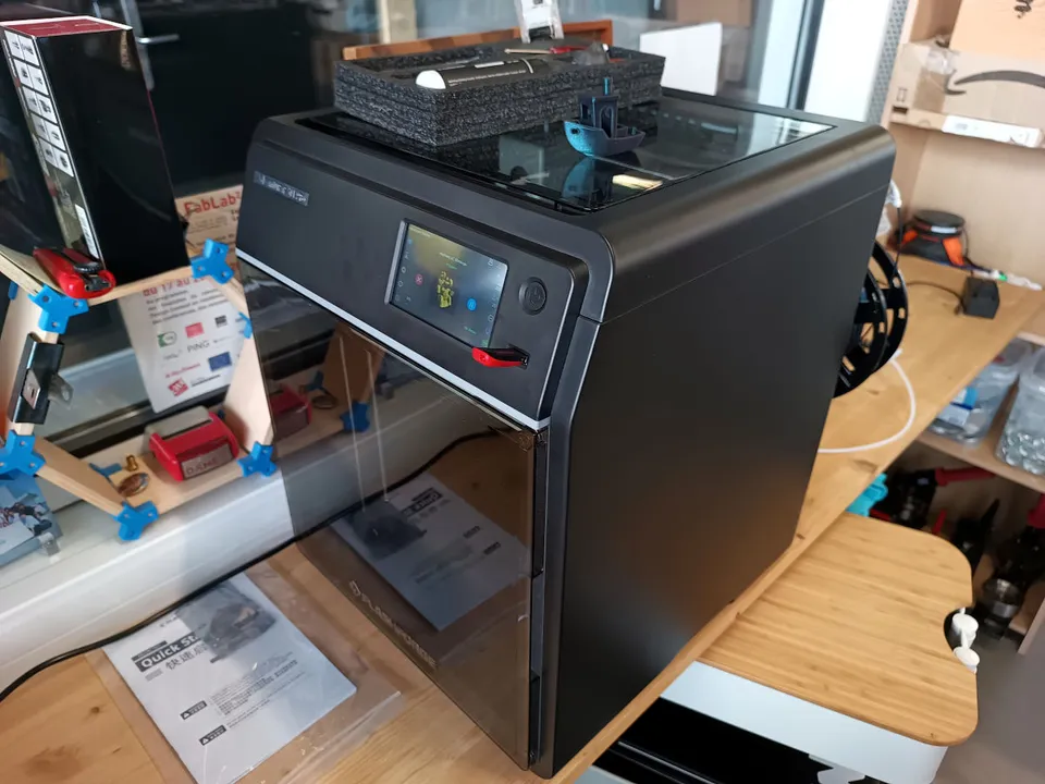 A newly arrived Flashforge Adventurer 5M Pro enclosed printer on a fab lab bench, with a printed boat on its glass lid.