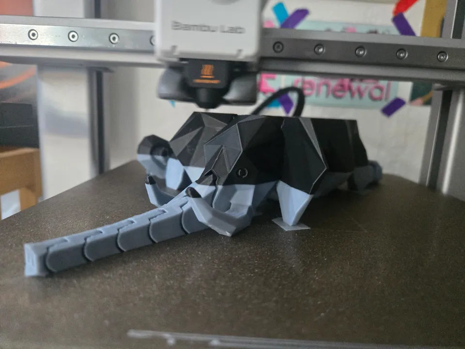A two-tone gray and black elephant model on the textured build plate of a Bambu Lab A1, with the printer's white toolhead on the rail above it.