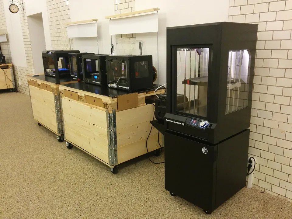 A tall MakerBot Replicator Z18 with its enclosed build chamber, standing beside a row of smaller MakerBot Replicator desktop printers.