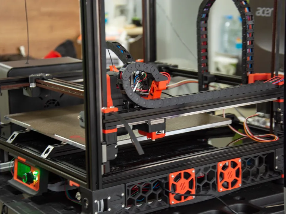 A self-built Voron 3D printer in an open aluminum frame, its orange toolhead on the gantry above the build plate.