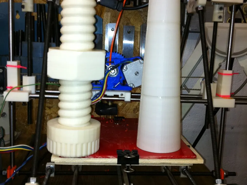 A home-built RepRap-style printer with two large white prints on its bed: an oversized bolt and nut, and a tall tapered cone made of three prints stacked and joined.