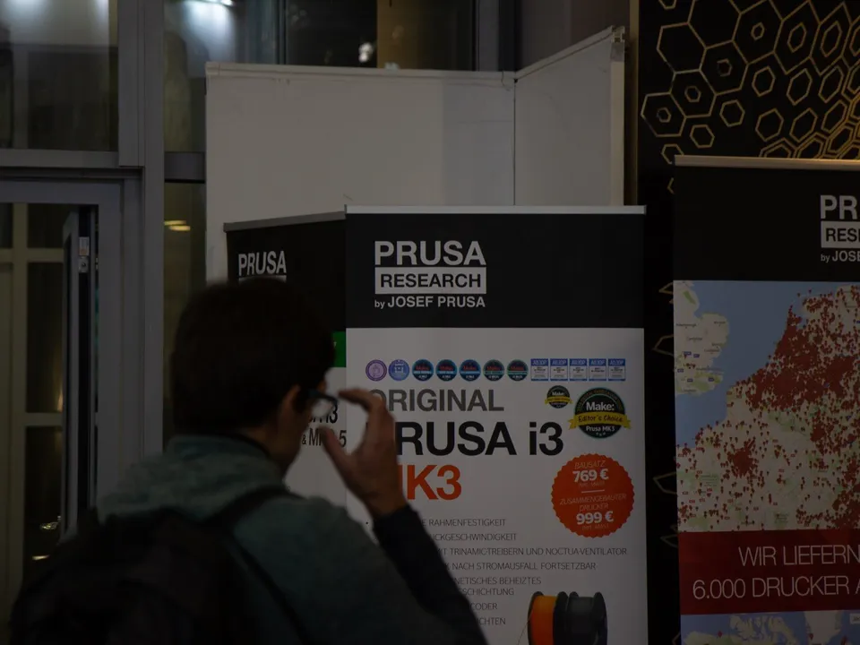 A visitor at the Formnext 2018 trade fair in Frankfurt faces a Prusa Research banner for the Original Prusa i3 MK3, its round price badge reading 769 € for the kit and 999 € assembled.